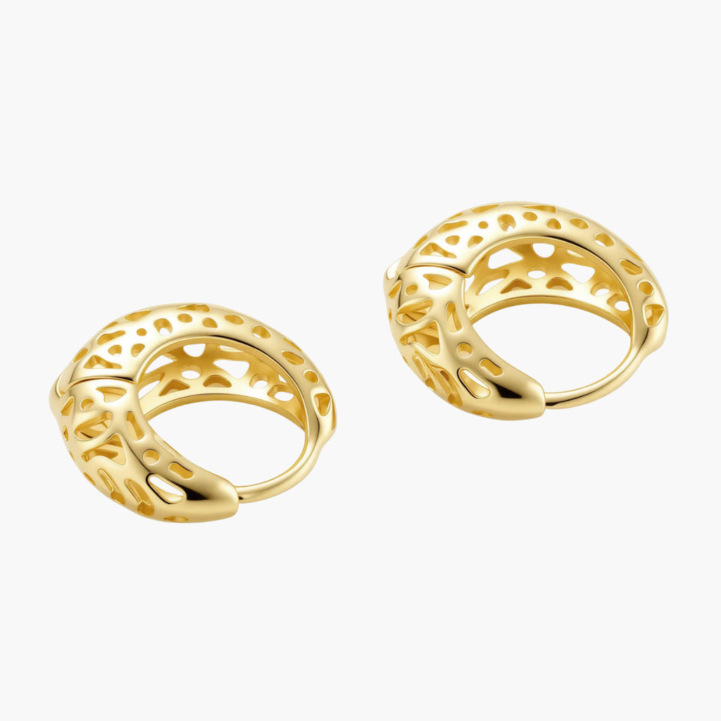 Close-up of small gold-plated hoop earrings with intricate honeycomb cutout pattern on cream background.