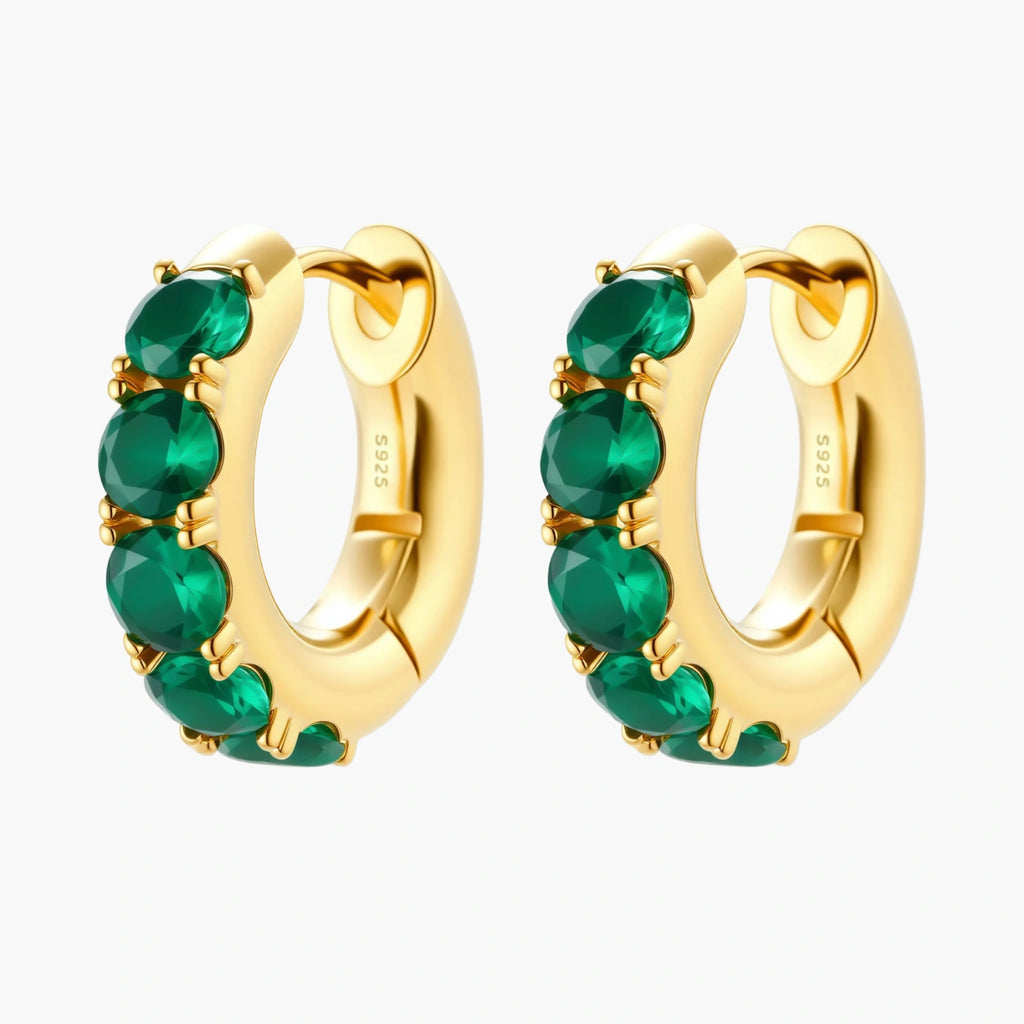 Close-up of gold-plated huggie hoop earrings featuring four emerald green cubic zirconia stones on white background.