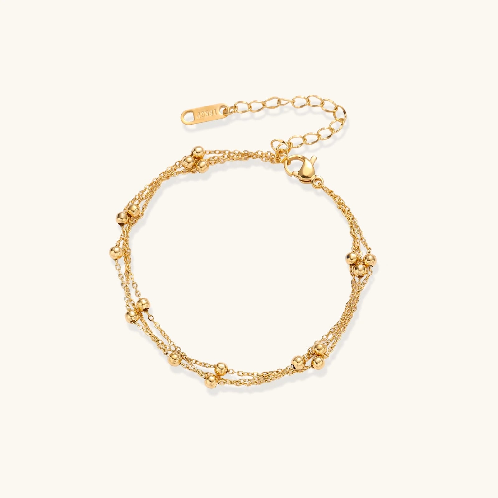 Three-strand gold-plated bracelet with clustered ball beads and adjustable clasp on cream background