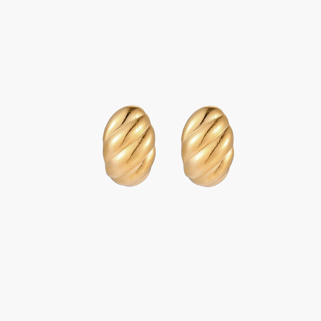 Chunky gold twisted rope huggie hoops with diagonal grooves and high-polish finish on cream background