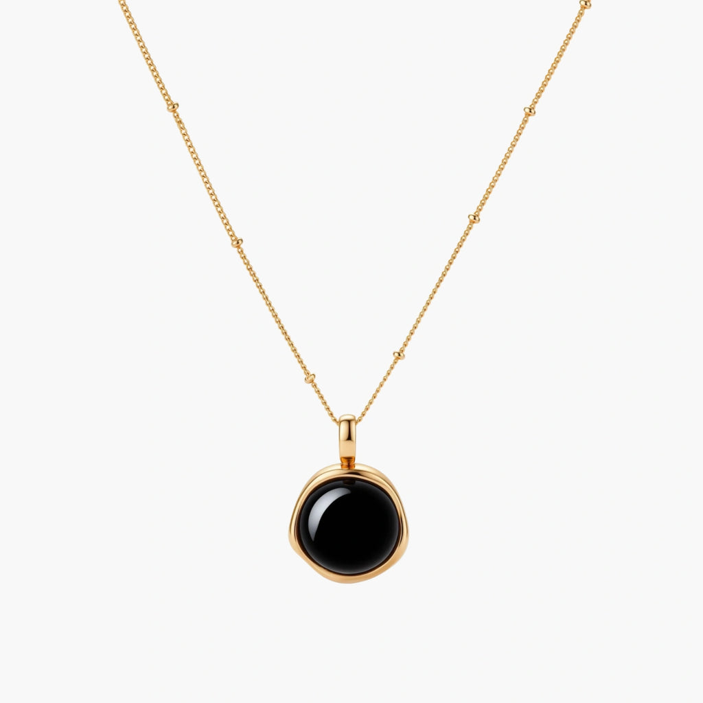 Circular black agate pendant on gold-plated sterling silver chain against cream background, showing modern minimalist design.