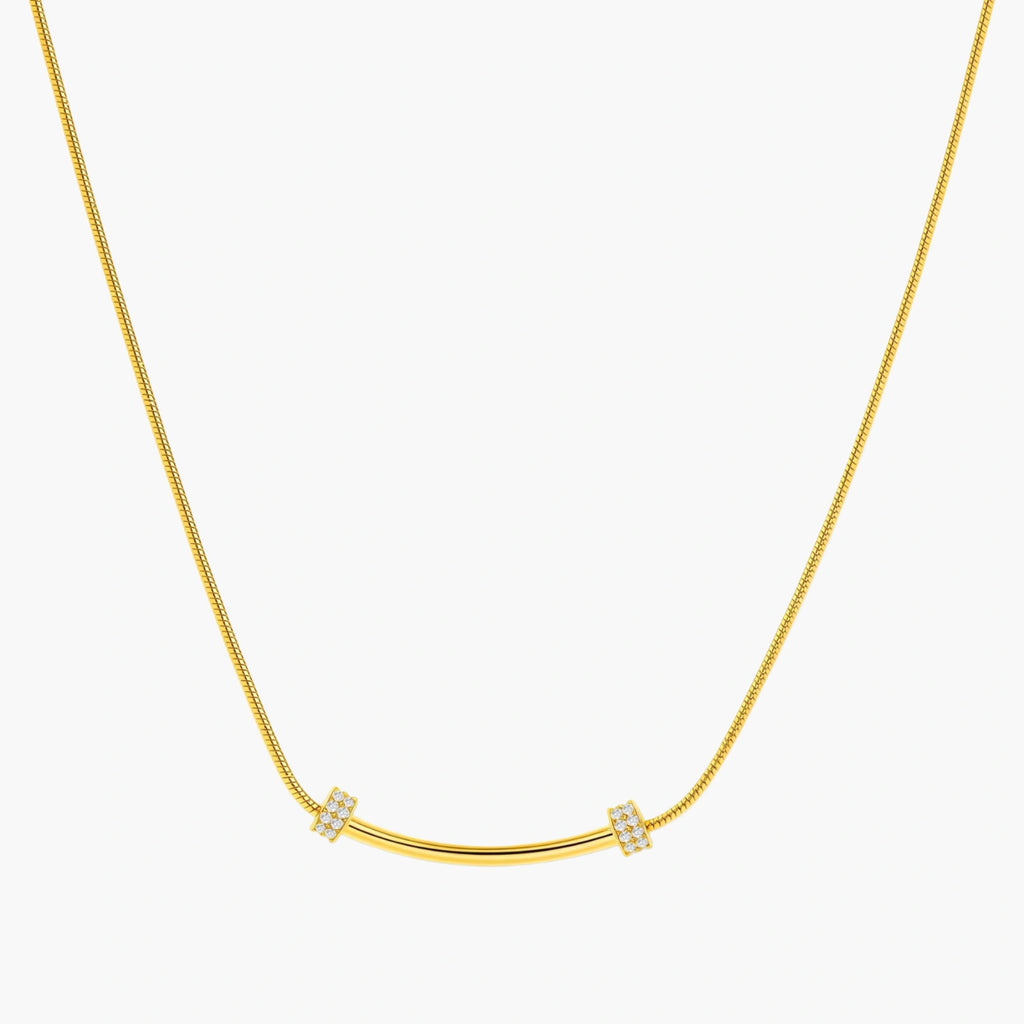 Delicate gold-plated necklace with curved bar pendant and crystal accents on snake chain against cream background.