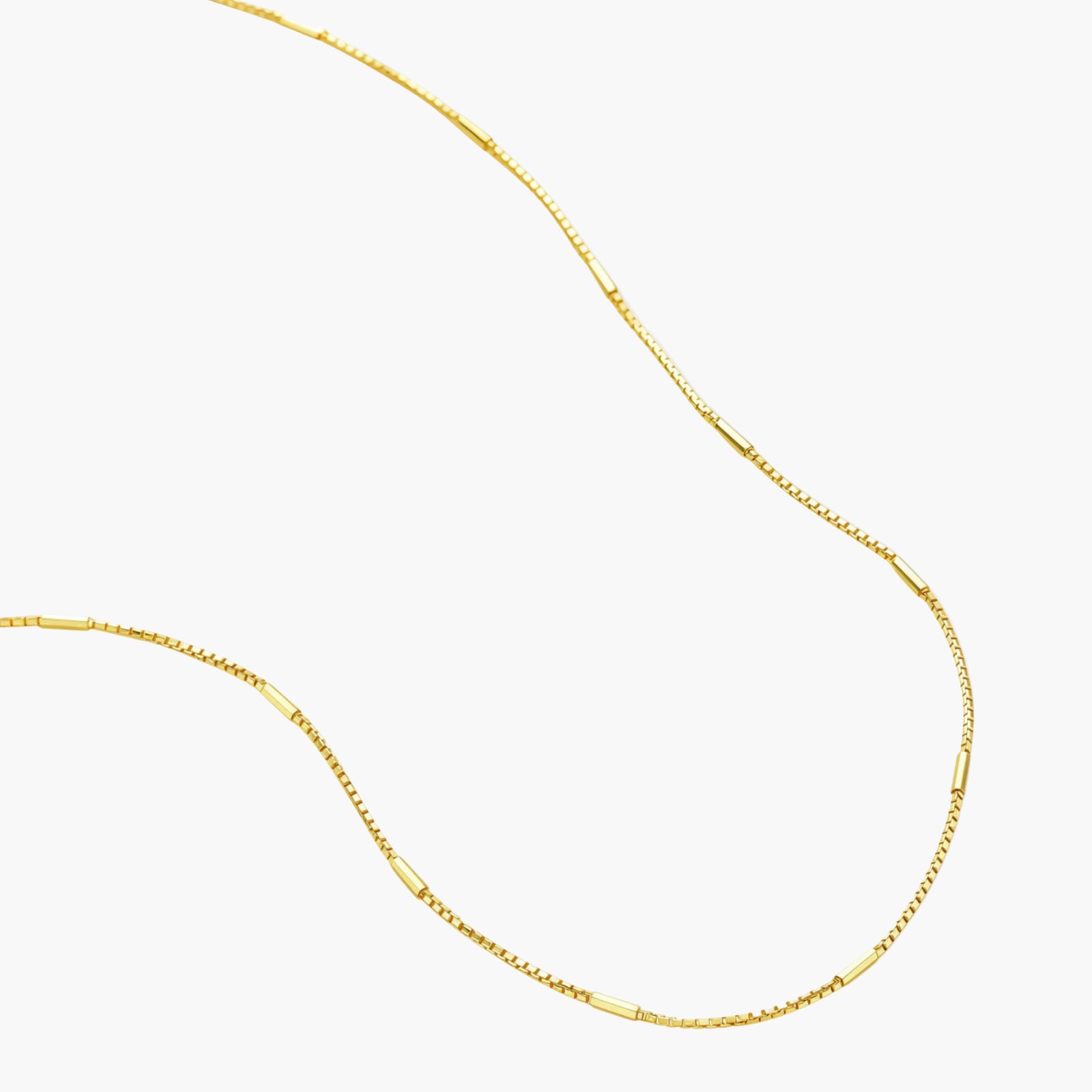 Delicate gold-plated sterling silver chain necklace with geometric segments displayed against cream background