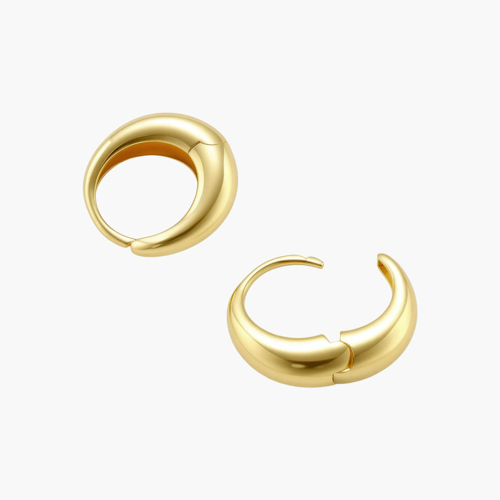 Chunky gold-plated sterling silver huggie hoop earrings with hinged closure mechanism on cream background.