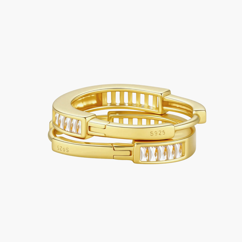 Close-up of gold-plated sterling silver huggie hoop earrings featuring rectangular cubic zirconia stones on neutral background.