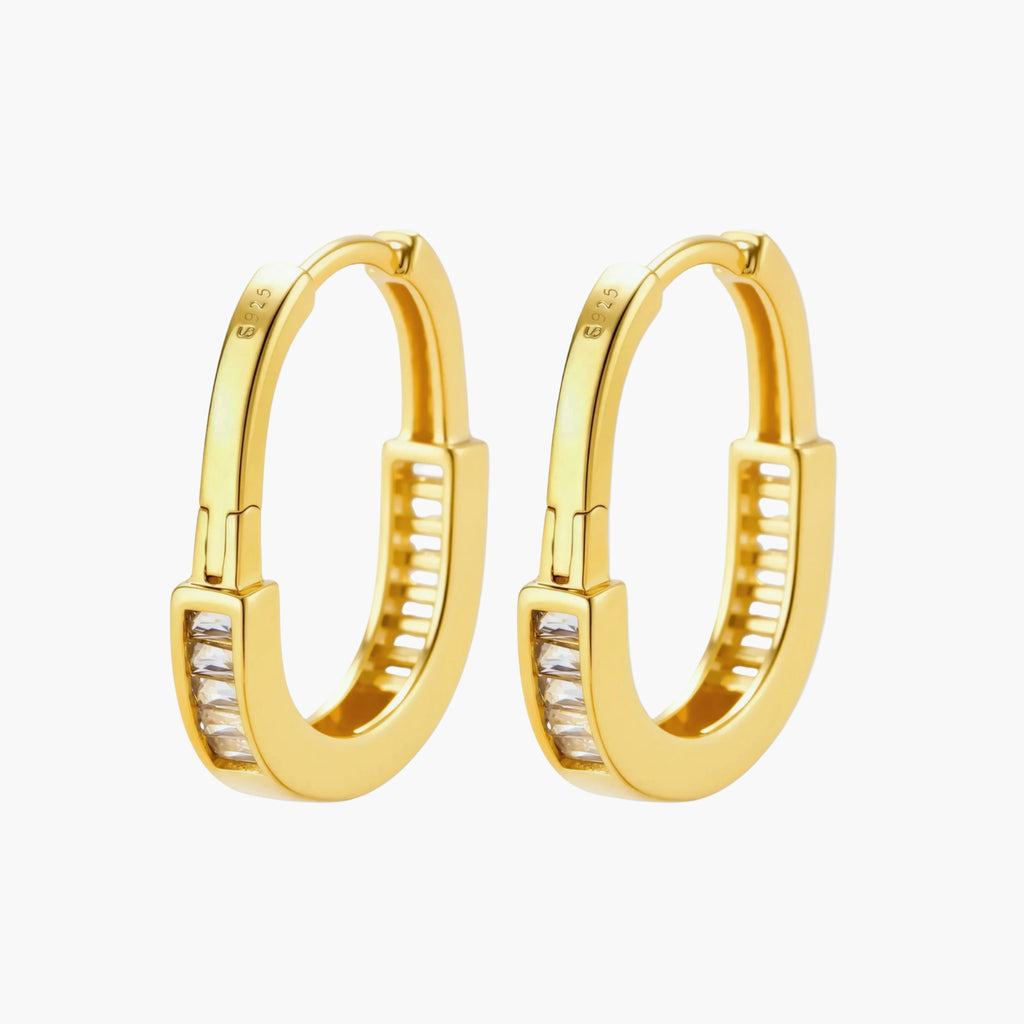 Close-up of gold-plated sterling silver huggie hoop earrings featuring rectangular cubic zirconia stones on neutral background.