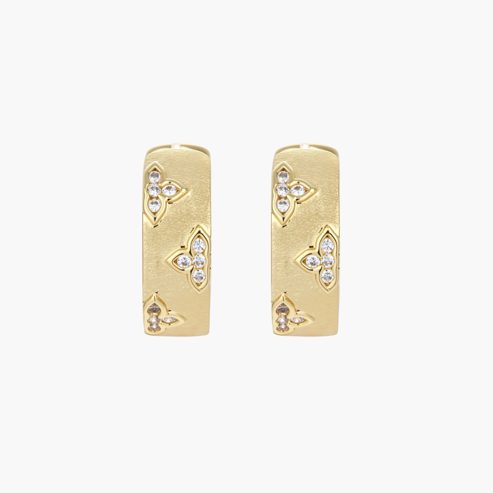 Gold-plated hoop earrings with textured surface and raised floral motifs set with clear zirconia stones on cream background.