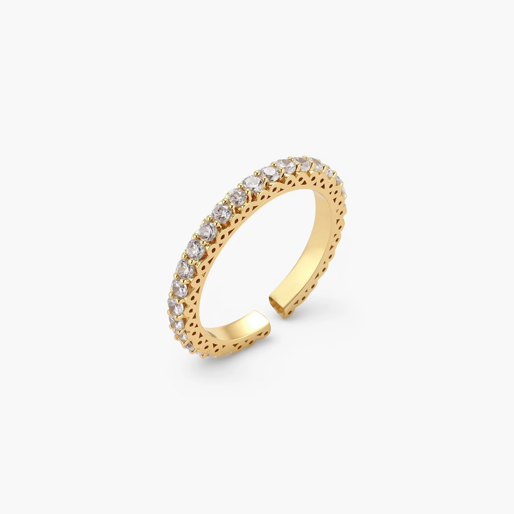 Close-up of adjustable gold-plated ring with continuous row of round zirconia stones on neutral background.