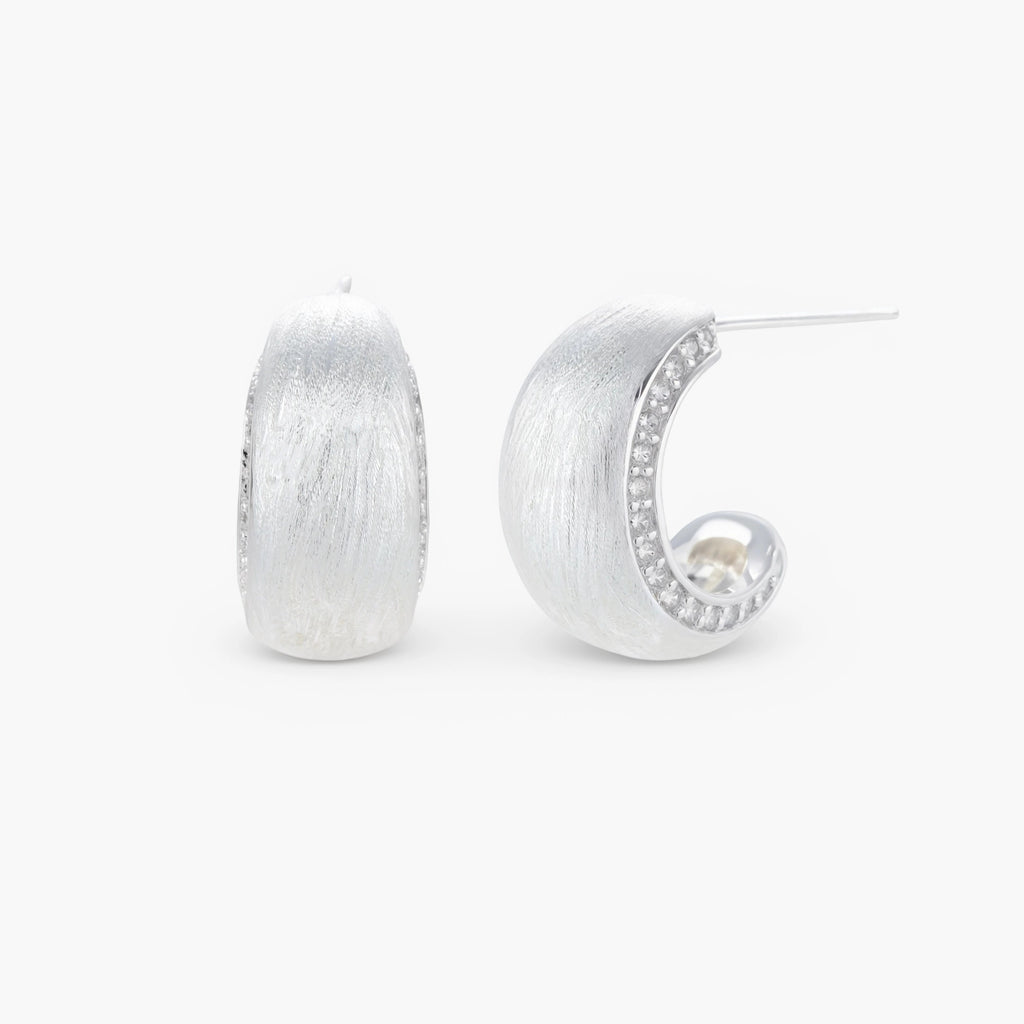 Close-up of small silver-plated hoop earrings with brushed texture and a row of sparkling zircon crystals on white background