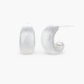 Close-up of small silver-plated hoop earrings with brushed texture and a row of sparkling zircon crystals on white background