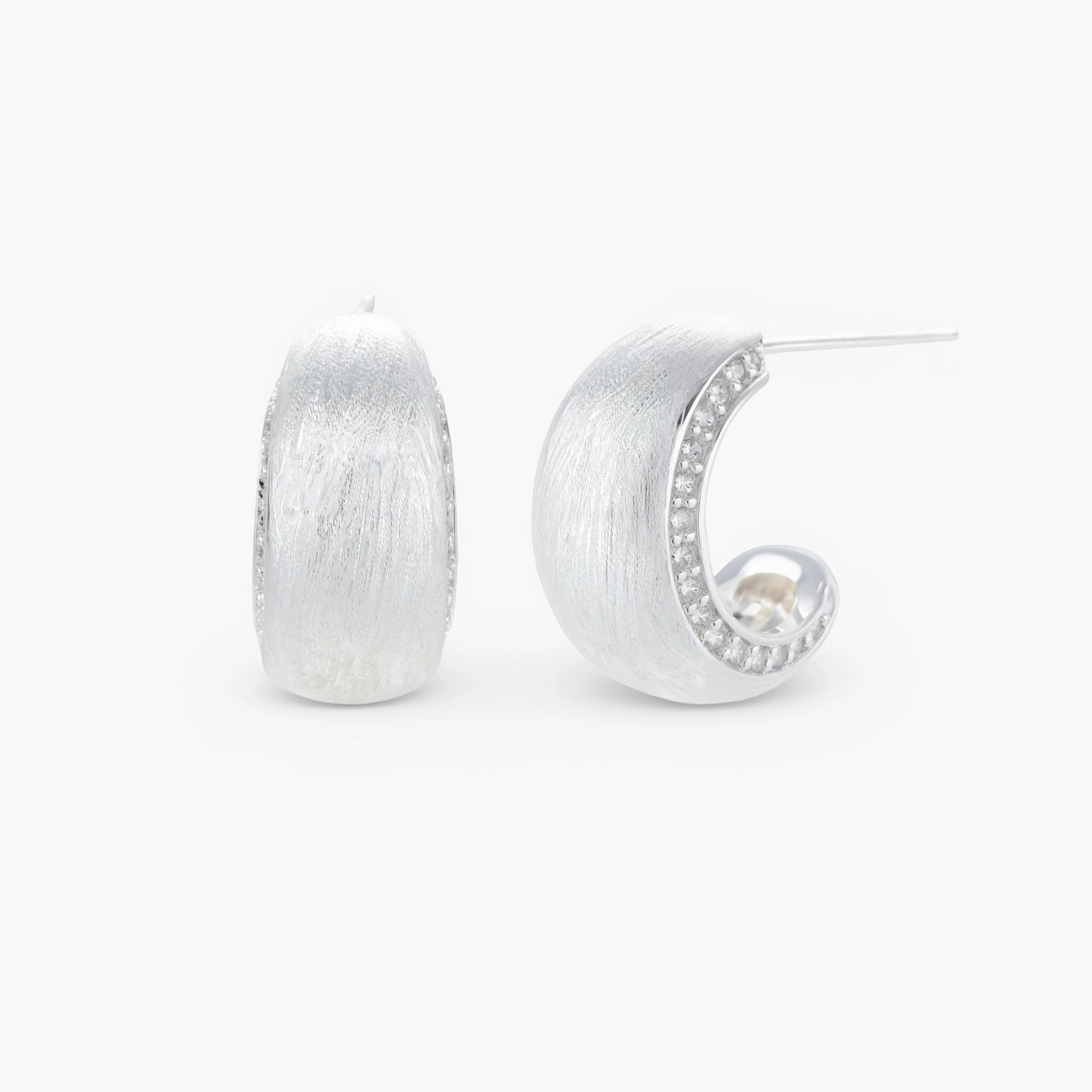 Close-up of small silver-plated hoop earrings with brushed texture and a row of sparkling zircon crystals on white background