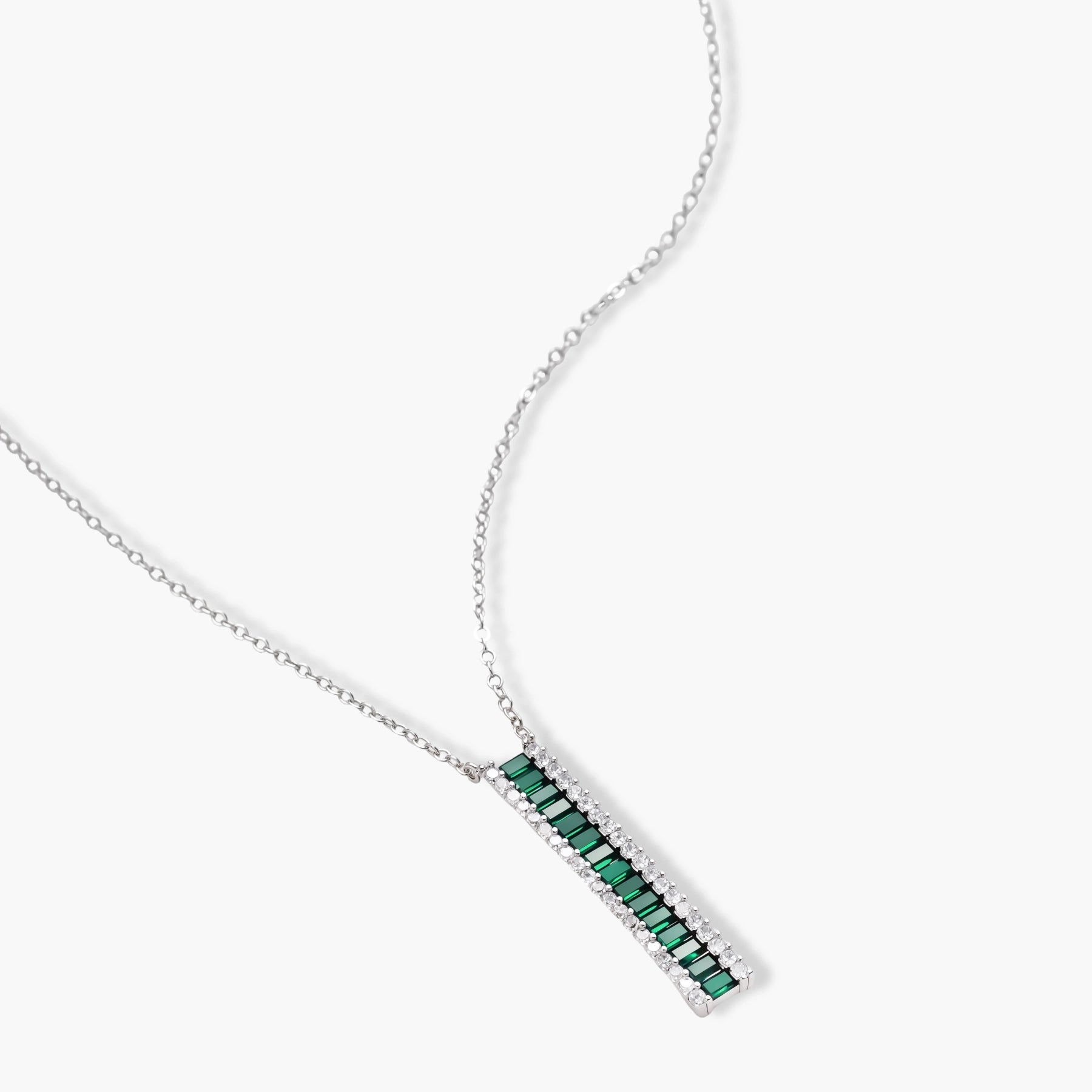 White gold plated jewelry set with emerald green rectangular stones and clear crystals in geometric rows on white background.