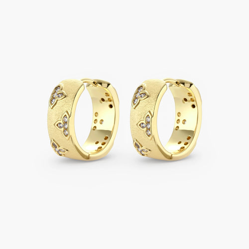 Gold-plated hoop earrings with textured surface and raised floral motifs set with clear zirconia stones on cream background.