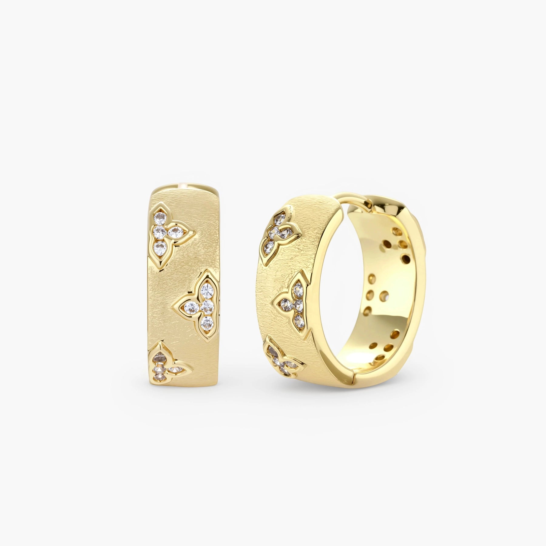 Gold-plated hoop earrings with textured surface and raised floral motifs set with clear zirconia stones on cream background.