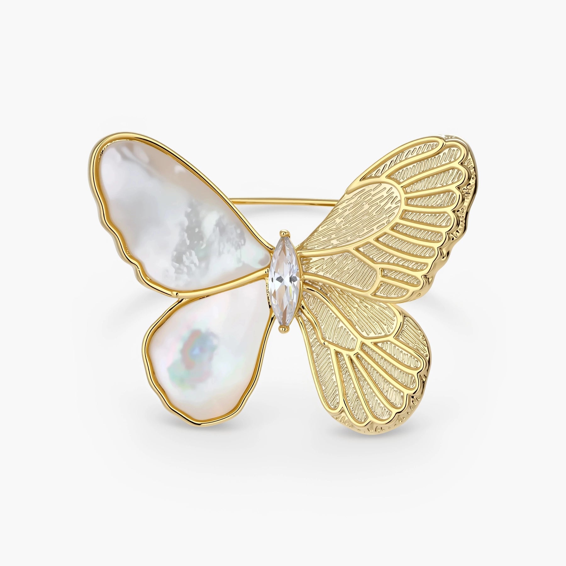 Gold-plated butterfly brooch with mother-of-pearl left wings, engraved gold right wings, and central zirconia crystal on cream background.