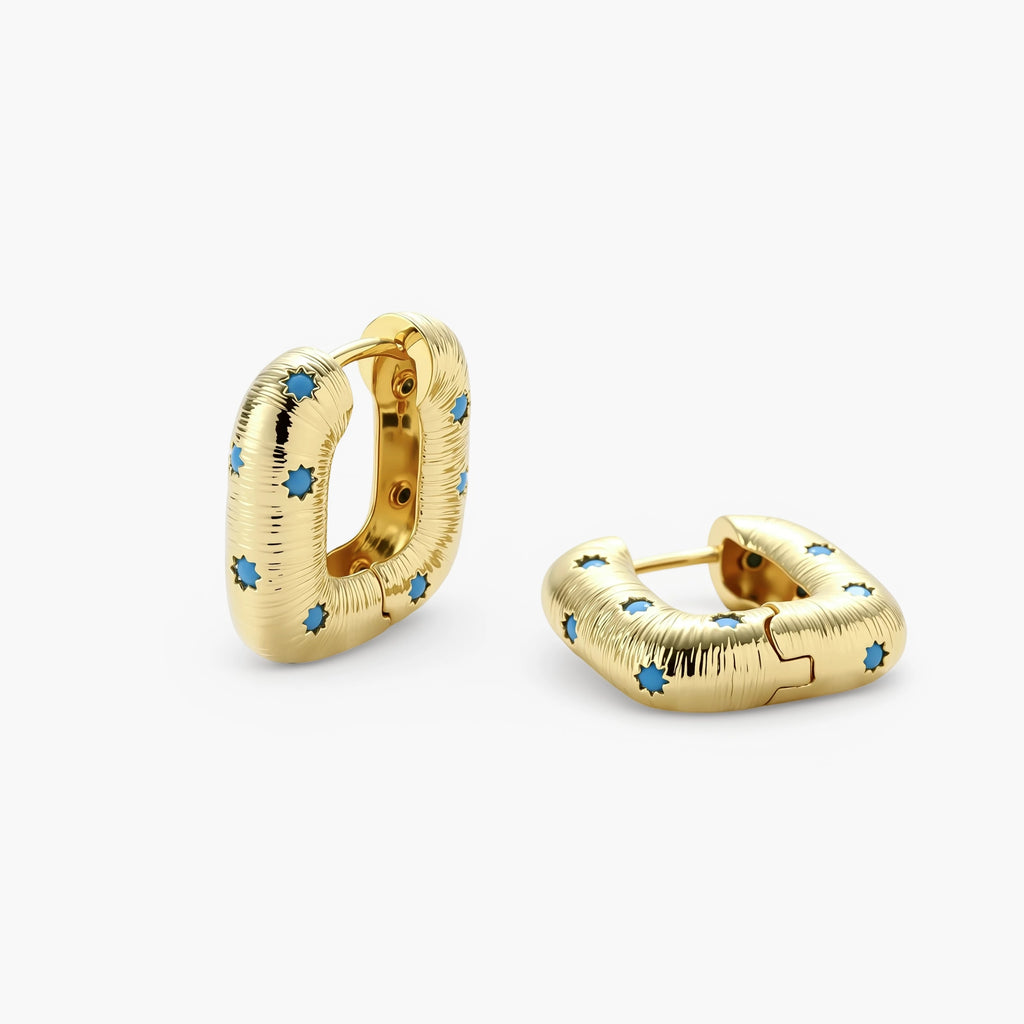 Gold-plated huggie hoop earrings with blue star inlays and textured surface, shown against white background.