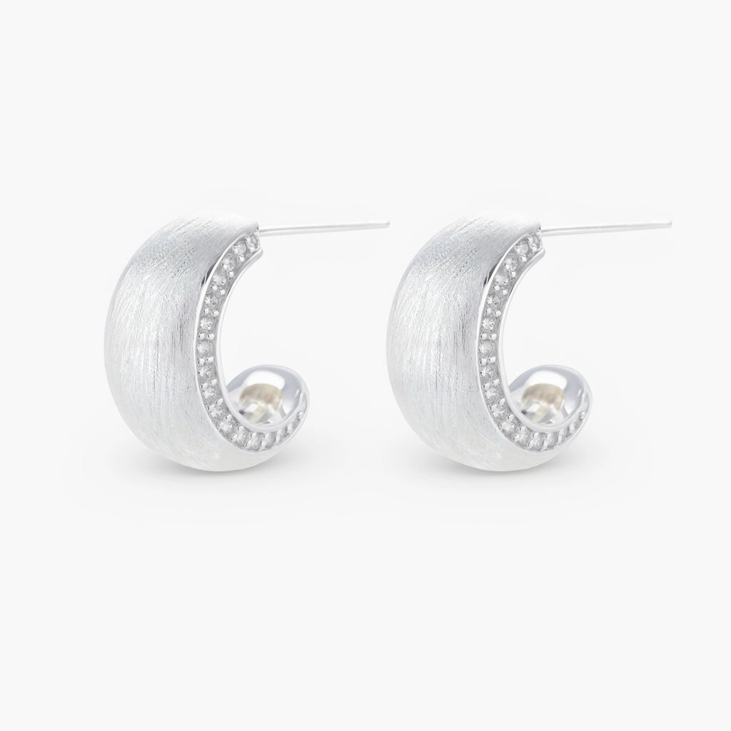 Close-up of small silver-plated hoop earrings with brushed texture and a row of sparkling zircon crystals on white background