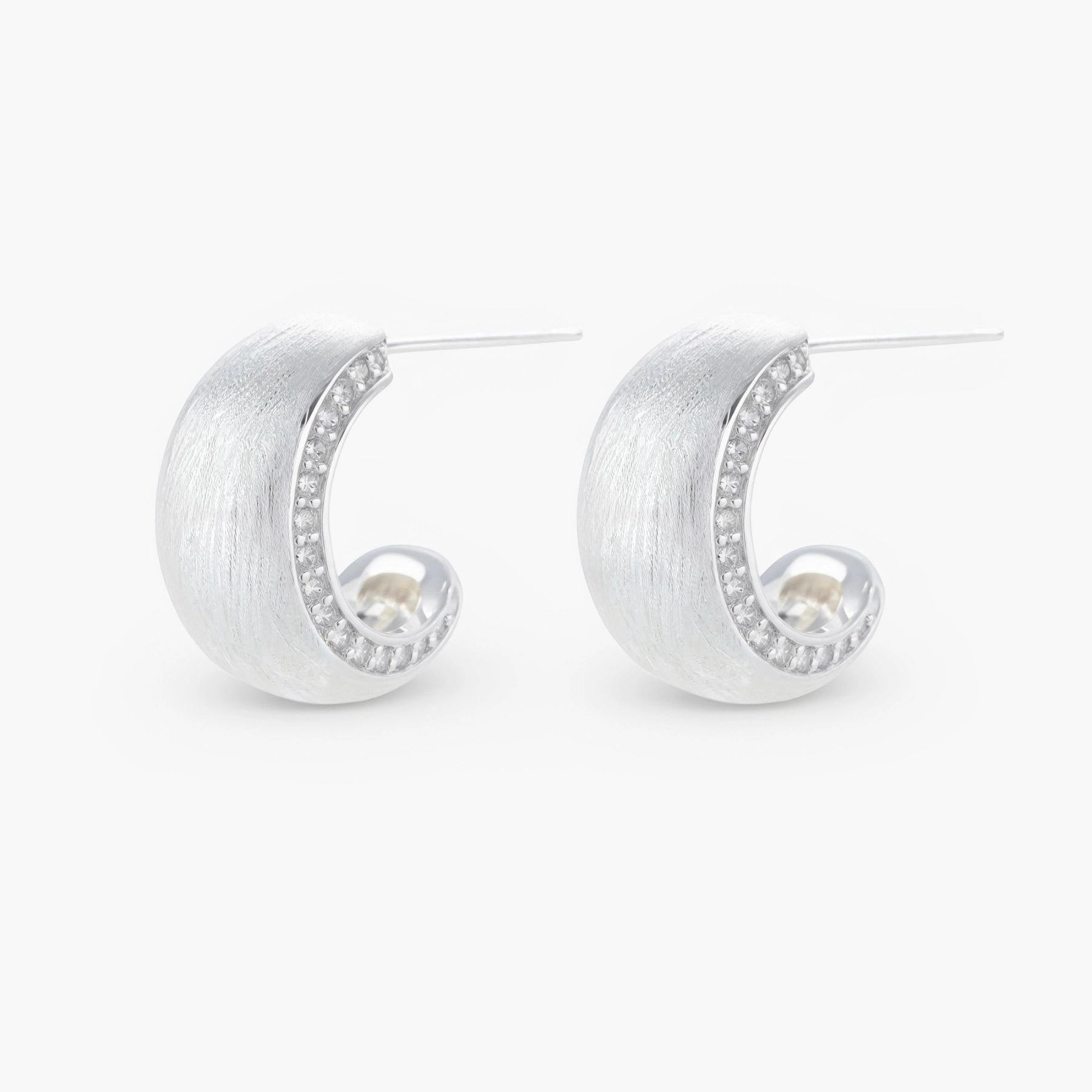 Close-up of small silver-plated hoop earrings with brushed texture and a row of sparkling zircon crystals on white background