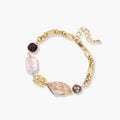 Gold-plated chain bracelet with mixed gemstones including purple stone, baroque pearl, and clear crystal on neutral background.
