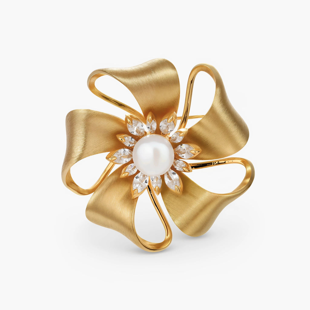 18K gold-plated bow brooch with dimensional ribbon design, pearl center, and sparkling zircon stones on white background.