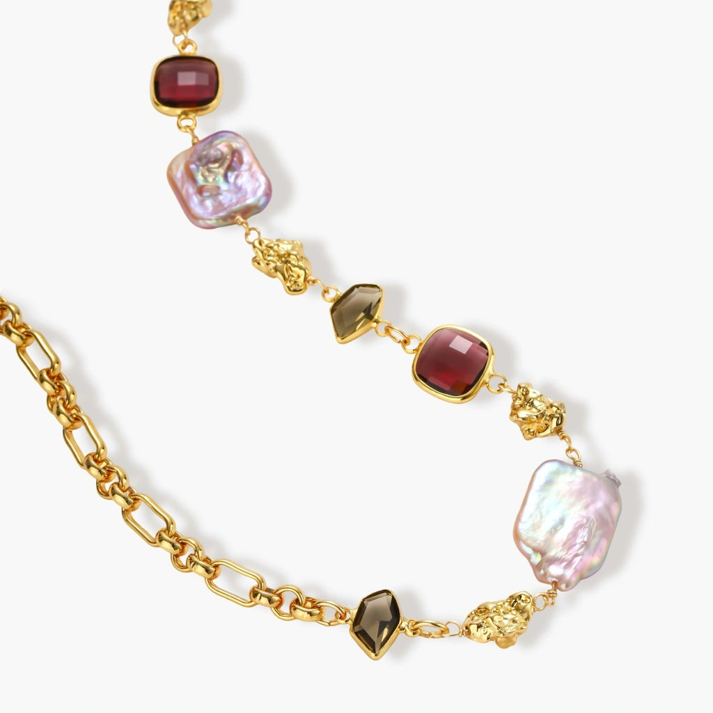 18k gold-plated chain necklace with iridescent baroque pearls and burgundy gemstones on white background.